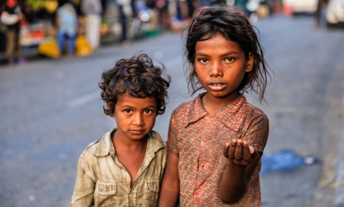 The Reality of Street Children in Pakistan: Why Thousands of Children Need Our Support 2 Two young children standing close together on a city street, with the older child holding out an open hand while looking directly at the camera.